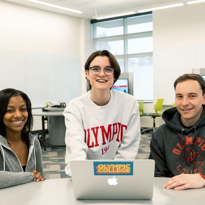 Three students sitting at a table in front of a laptop computer.