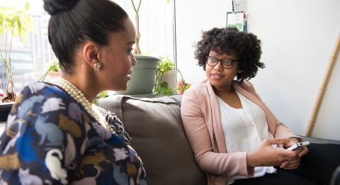 Two women sitting on couch speaking with each other